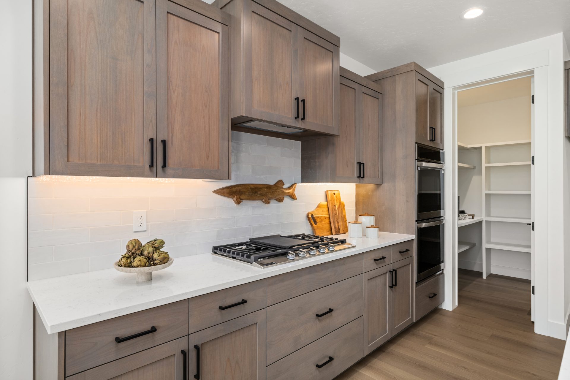 Kitchen with light hardwood flooring and a contemporary design. Kitchen with light hardwood flooring and a contemporary design. The space features wood cabinetry, white countertops, a tile backsplash, and a gas cooktop with a built-in range hood. A built-
