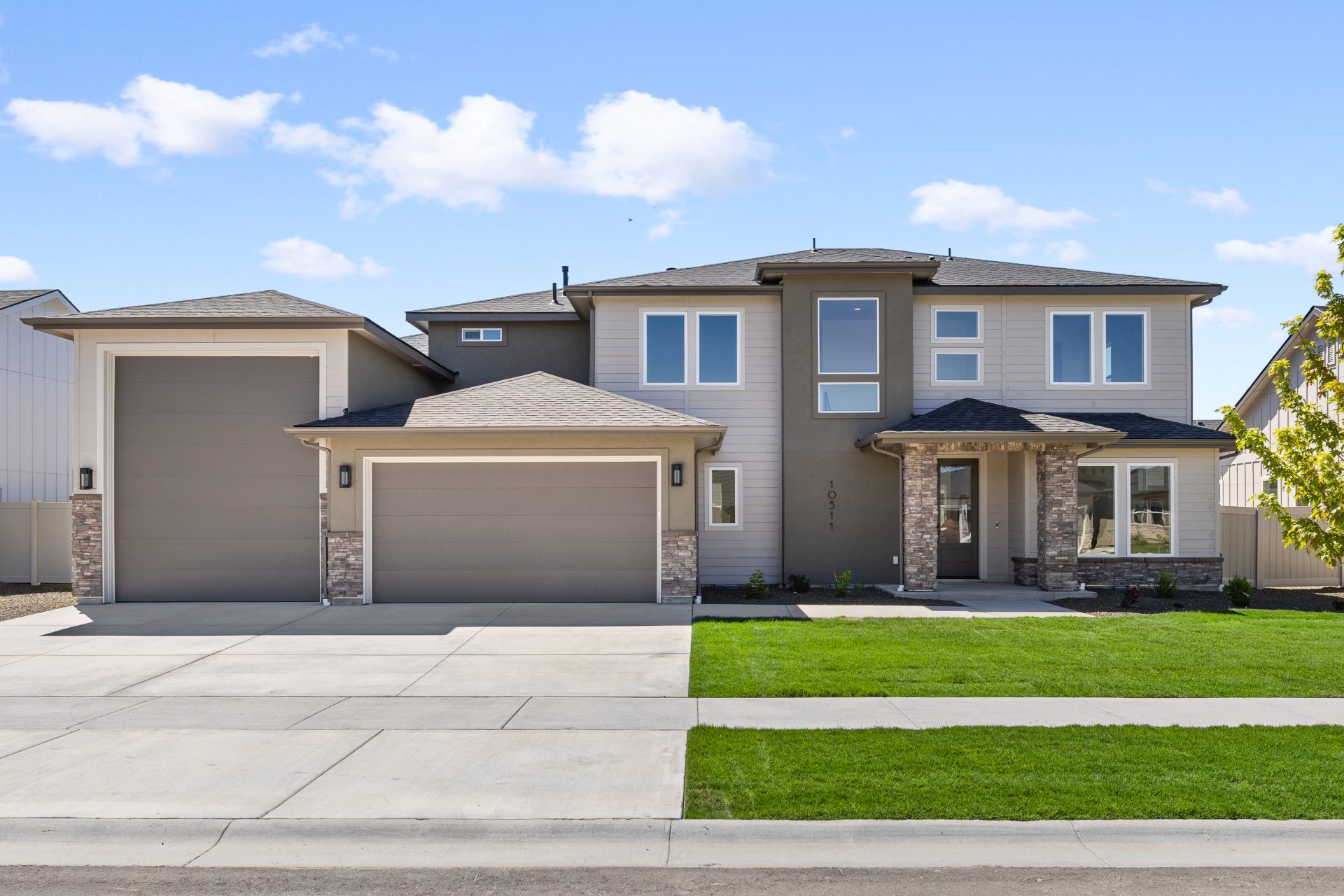 Two-story home with two-tone exterior in taupe and tan, featuring stone veneer accents, mixed siding textures, and a contemporary design. Two-story home with two-tone exterior in taupe and tan, featuring stone veneer accents, mixed siding textures, and a 
